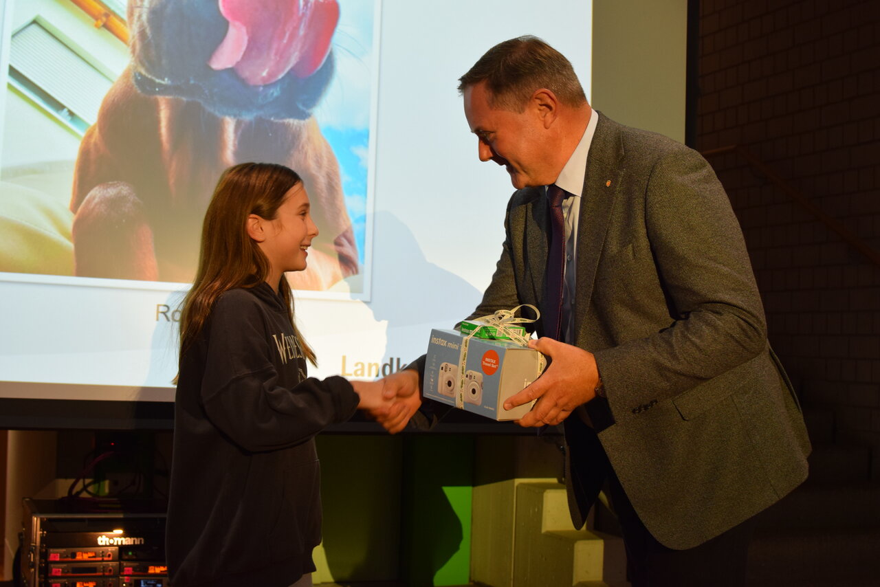 Landrat Bernd Obst übergibt Gewinnerin des Kinderfotopreises einen Preis.