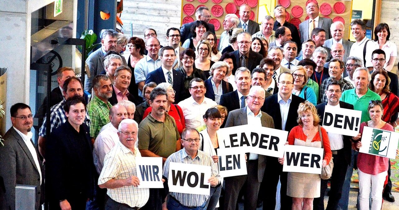 Heterogene, motivierte Gruppe Menschen hält Schilder mit den Worten "Wir wollen LEADER Region werden" hoch. Abbild der Auftaktveranstaltung.