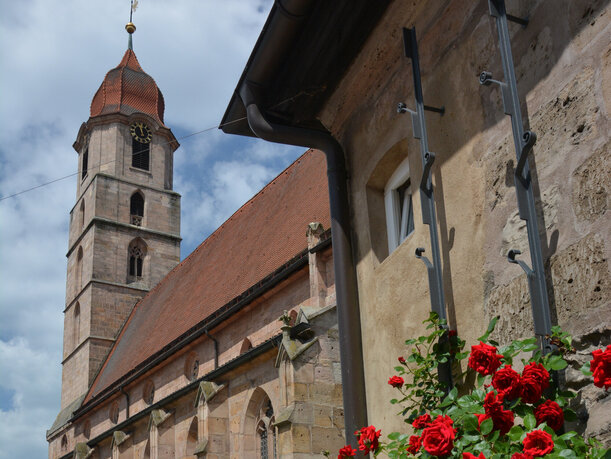 Das Bild zeigt den Klosterhof in Langenzenn. Im Vordergrund sind rote Rosen zu sehen. 