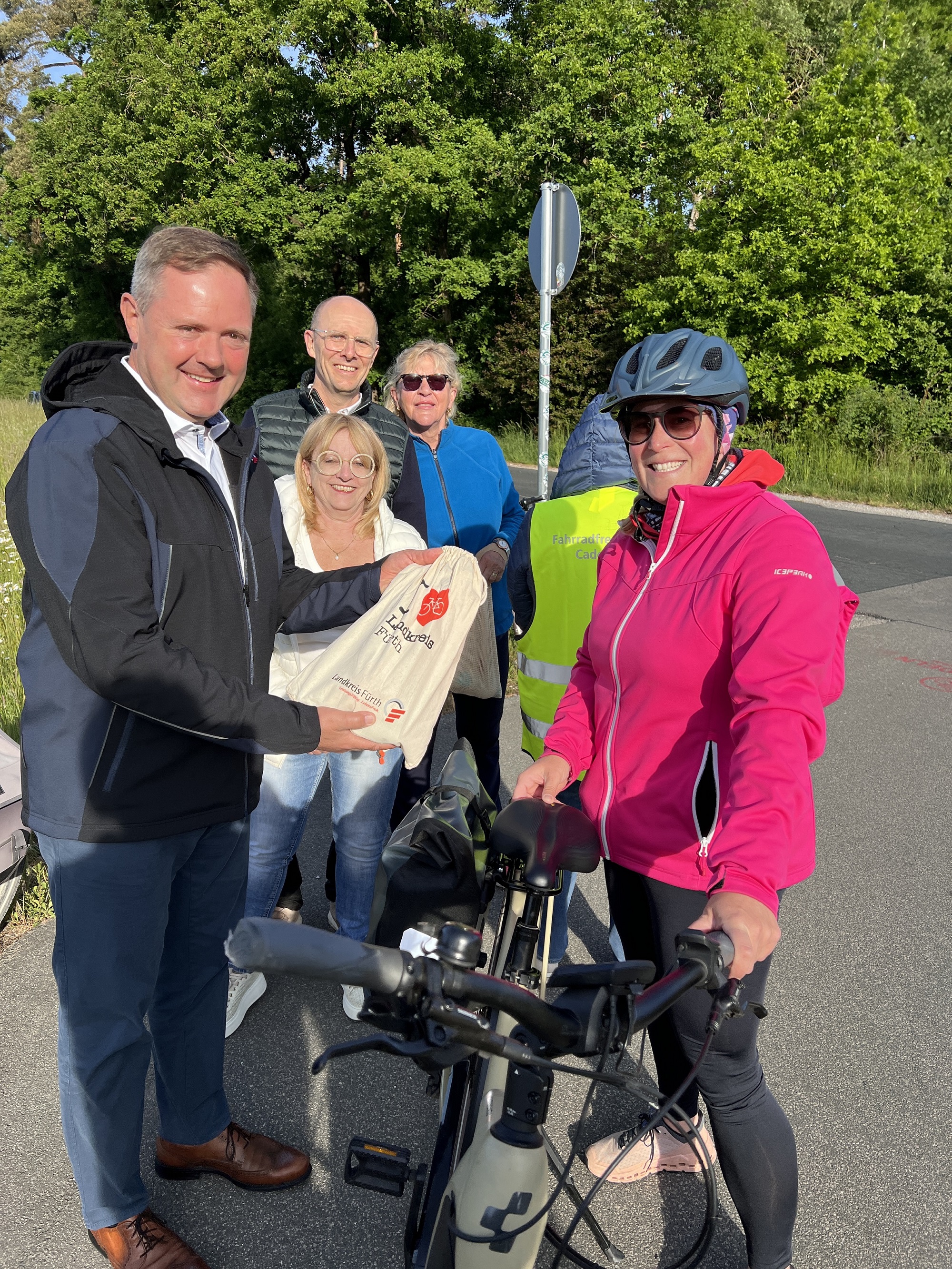 Landrat Bernd Obst übergibt am Radweg in Wachendorf eine gesunde Frühstückstüte an eine sichtlich erfreute Radfahrerin.
