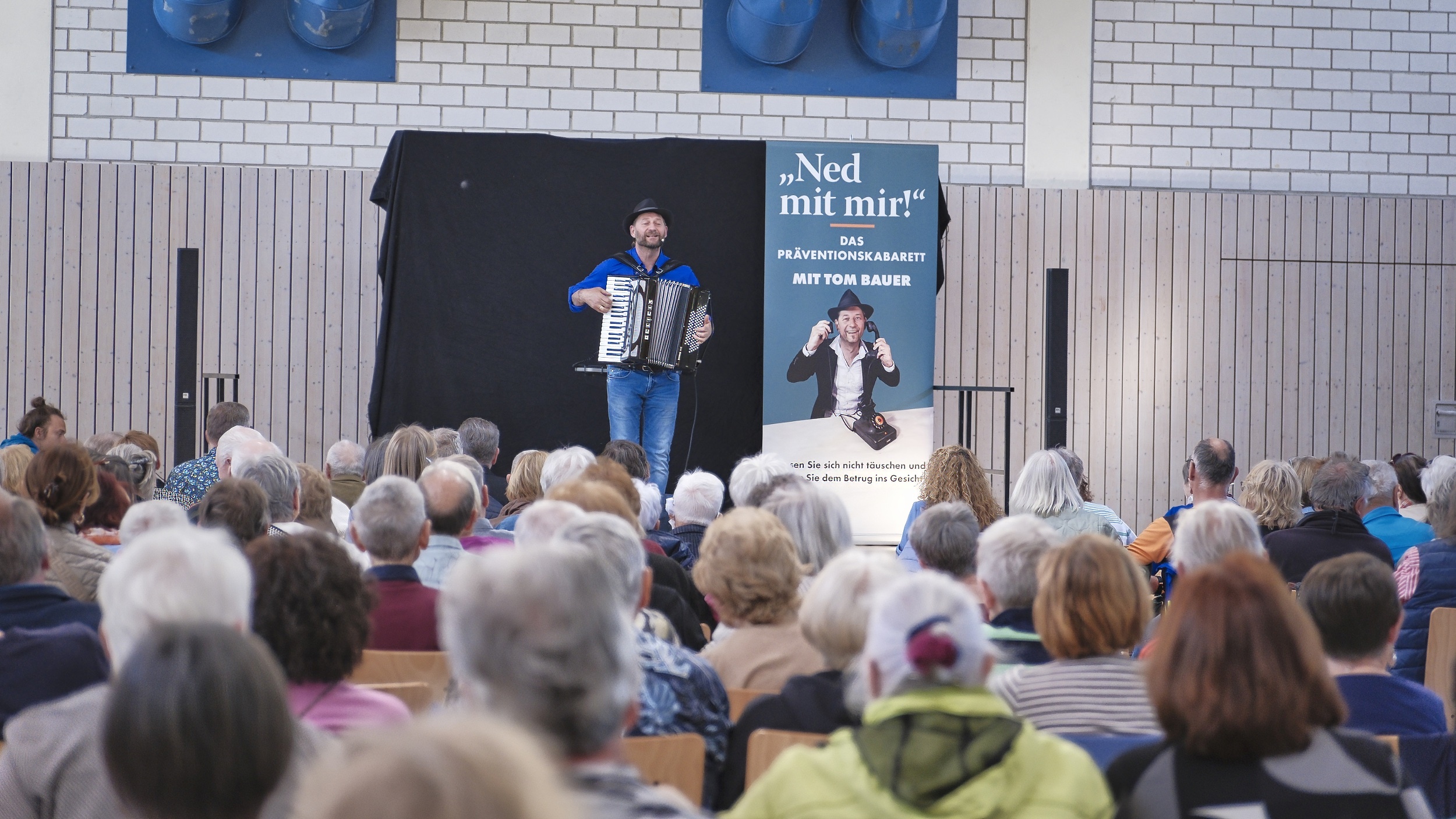 Eine Person steht auf der Bühne. Davor sitzt ein älteres Publikum